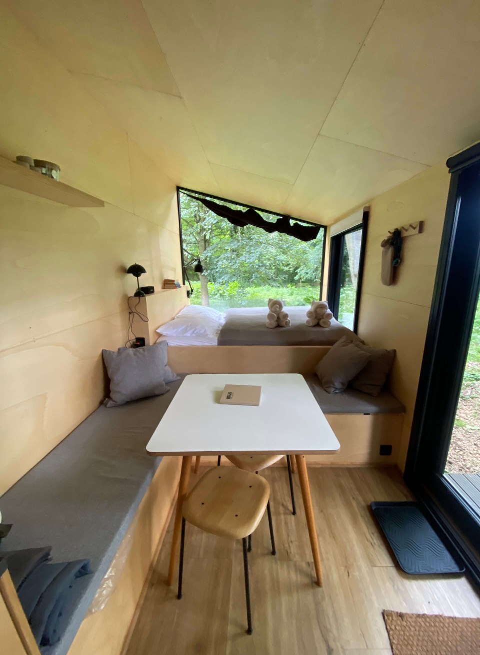 Licht interieur van een Tiny House op Schloss Neuhoff met gezellige zithoek, bed en uitzicht op het bos.