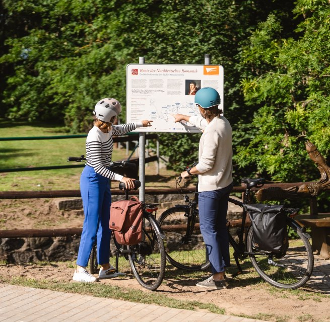 Twee fietsers staan bij het bord voor de Route van de Noord-Duitse Romantiek // Frauke en Wolf vinden op belangrijke punten langs de route informatie over de schilders en de regio. // © MV-T/Gross Twee fietsers staan bij het bord voor de Route van de Noord-Duitse Romantiek