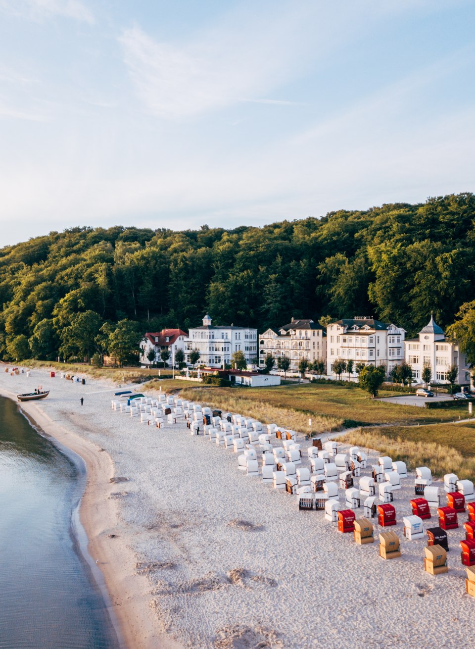 Plaża rybacka w Binz z leżakami, piaszczystą plażą i zabytkową architekturą spa przed zalesionym wzg&oacute;rzem.
