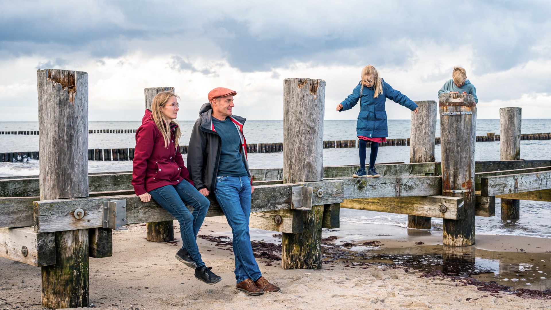 Family at an old wooden scaffolding for a pier on the beach in Kühlungsborn - the children are doing gymnastics on it.