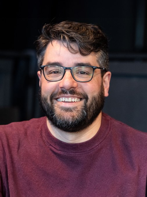 Portrait photo of assistant director Georg Meier in a wine-red sweater against a dark background., © Peter van Heesen Portrait photo of assistant director Georg Meier in a wine-red sweater against a dark background., © Peter van Heesen