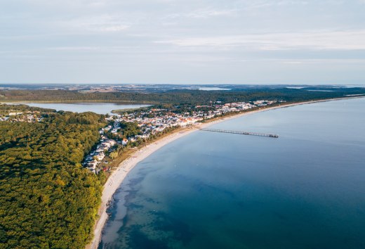 Aerial view of Binz on Rügen with pier, coastline and surrounding forests. // Aerial view of the Baltic seaside resort of Binz on the island of Rügen, which stretches along the curved coastline. The pier juts out into the calm, turquoise waters, while the town is surrounded by dense forests and lakes. The sky is clear and the peaceful landscape invites you to linger. // © MV-T/Friedrich Aerial view of Binz on Rügen with pier, coastline and surrounding forests.