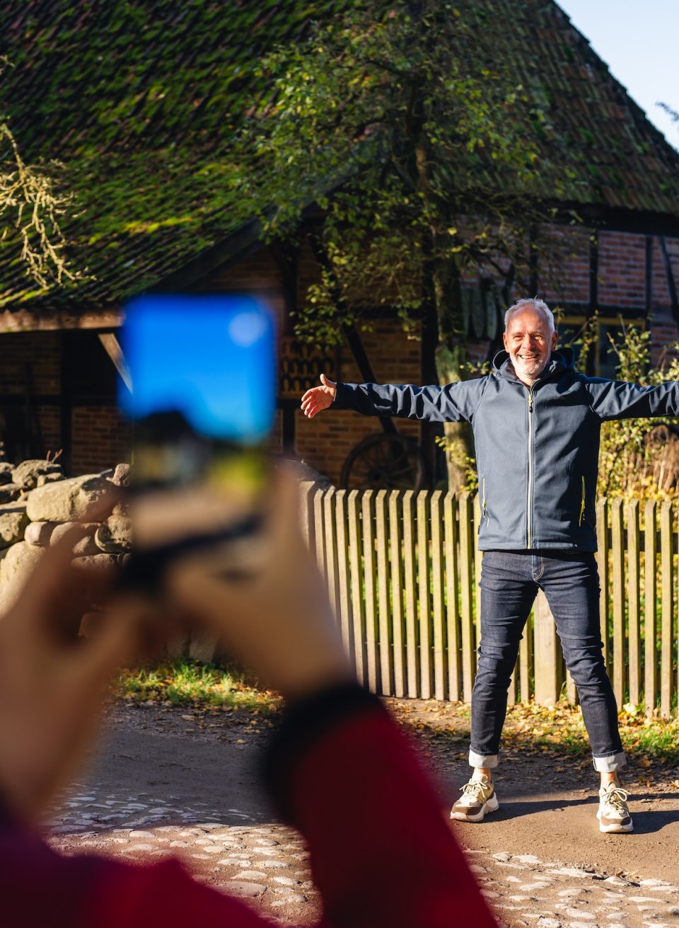 Een man poseert met uitgestrekte armen voor een historisch huis met rieten dak in het openluchtmuseum voor volkskunde Schwerin-Mueß.