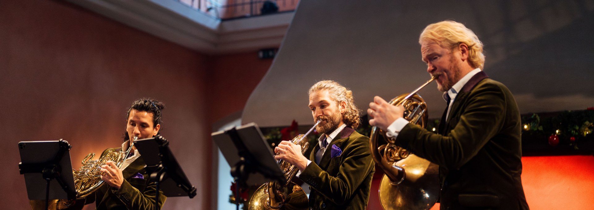 Three musicians from the horn quartet "german hornsound" play their French horns in the festively decorated hall of Ulrichshusen Castle.