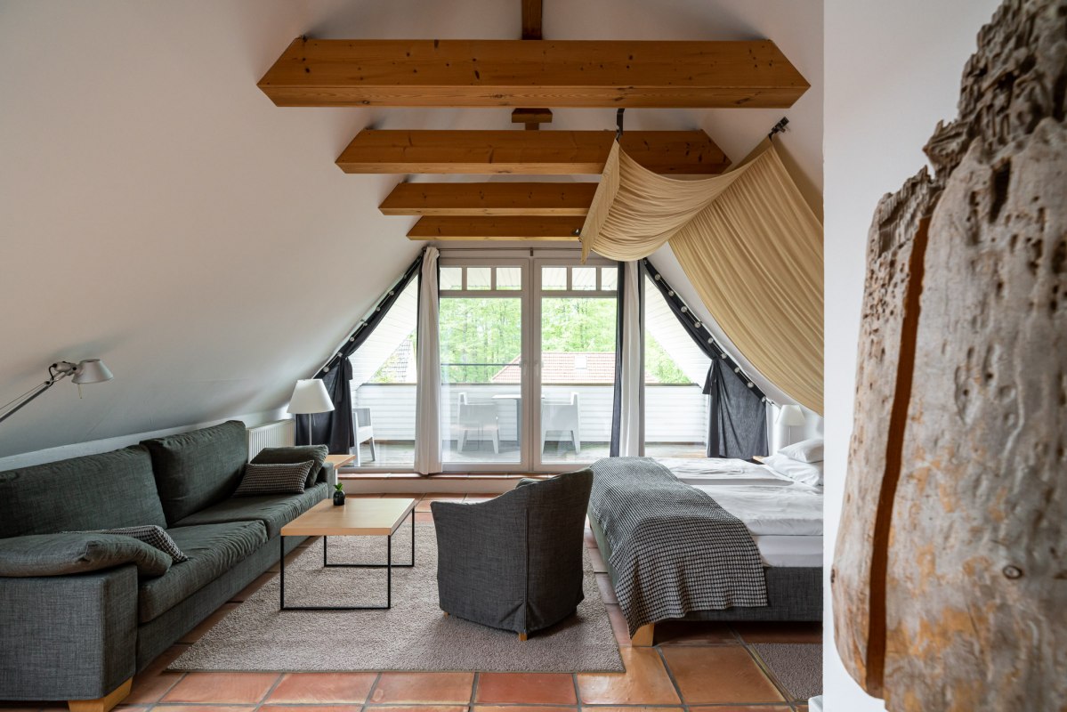 Een stijlvol ingerichte zolderkamer met zichtbare houten balken en een gezellige sfeer. De kamer biedt een comfortabele zithoek, een groot bed en toegang tot een balkon met uitzicht op het groen. Warme terracotta vloeren en lichtgekleurde stoffen maken het gezellige ontwerp af en nodigen uit om te ontspannen., &copy; Hotel Carpe Diem