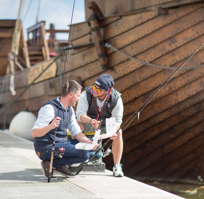 Young men fishing at the town harbor in Ueckermünde with a cog in the background., © TMV/Läufer