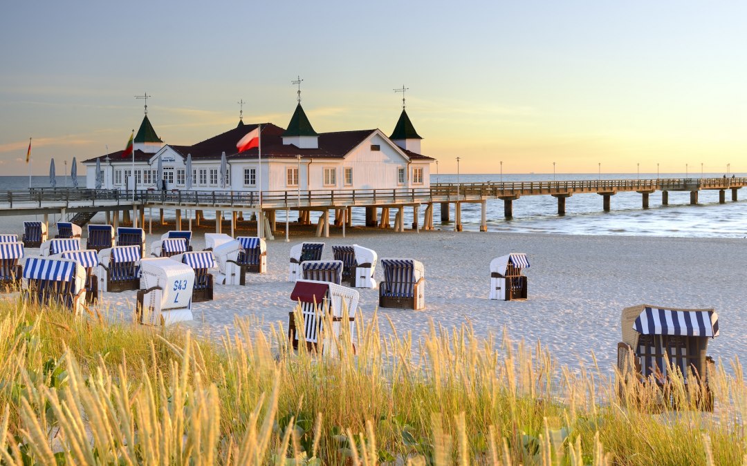 Strandstoelen staan langs het fijne zand van Ahlbeck, terwijl de historische pier de Oostzee in steekt. Warm avondlicht baadt de witte architectuur met groene torentjes in gouden tinten - een plek om diep adem te halen en aan te komen op het Baltische eiland Usedom. // &copy; Francesco Carovillano