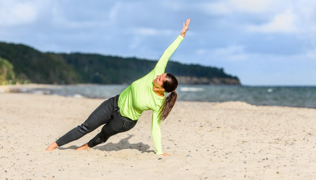 Podparcie boczne z unoszeniem ramion angażuje mięśnie całego ciała., © TMV/Tiemann Boczne podparcie na piasku z uniesieniem ramion angażuje mięśnie całego ciała.