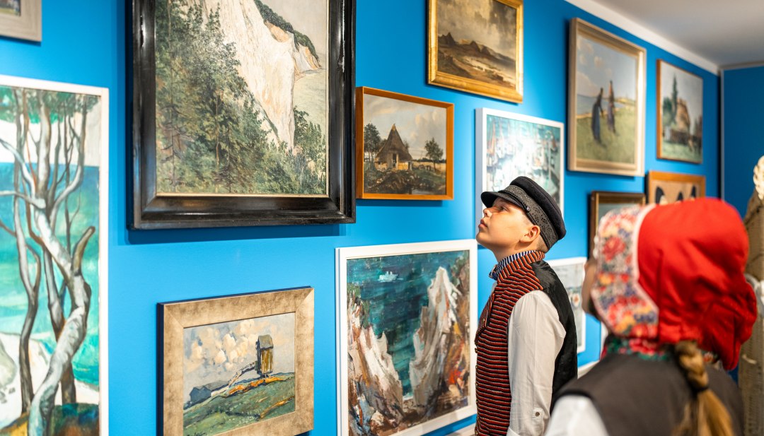 In het streekmuseum van Mönchgut hangen tekeningen en schilderijen aan de muur - kinderen staan er in traditionele kleding voor en bestuderen ze.