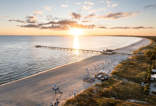 Luchtfoto van de pier van Ahlbeck bij zonsopgang, het strand en de Oostzee in een gouden gloed. // Zonsopgang boven de Oostzee, de pier van Ahlbeck strekt zich uit in het licht – het toneel voor een huwelijksbelofte met een weids uitzicht. // © MV-T/Gross Luchtfoto van de pier van Ahlbeck bij zonsopgang, het strand en de Oostzee in een gouden gloed.
