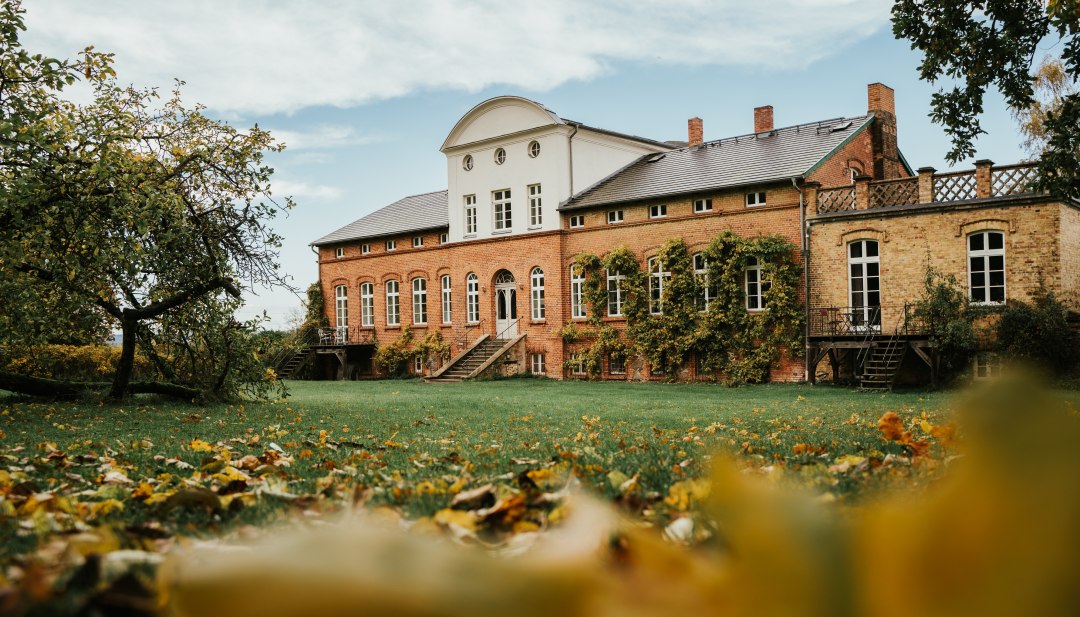 Bakstenen landhuis met wijngaarden en open trappenhuis in een herfstig parklandschap in West-Pommeren onder een licht bewolkte hemel.