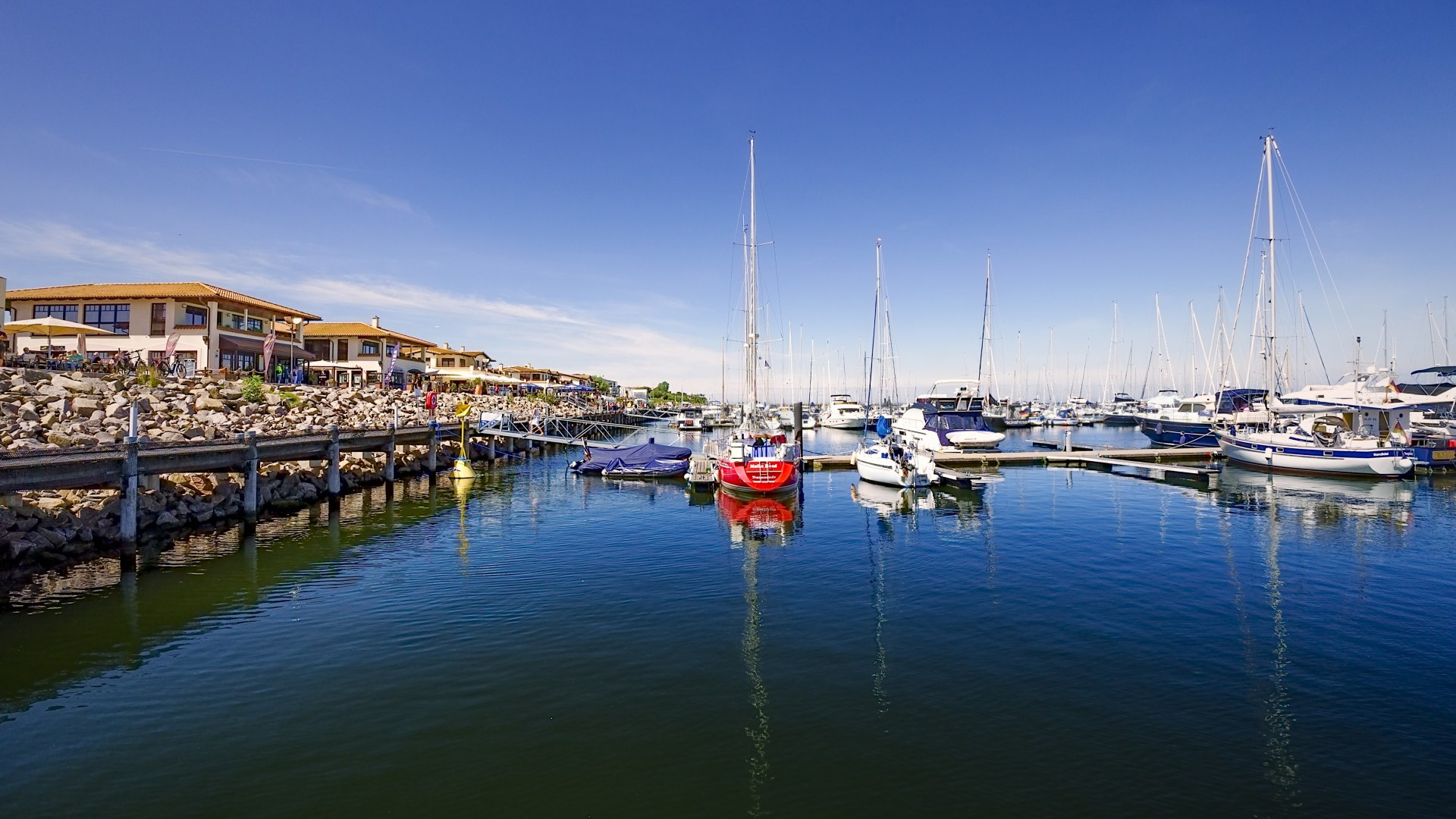 Uitzicht op de jachthaven van Kühlungsborn met zeilboten, promenade en restaurants bij helder weer.