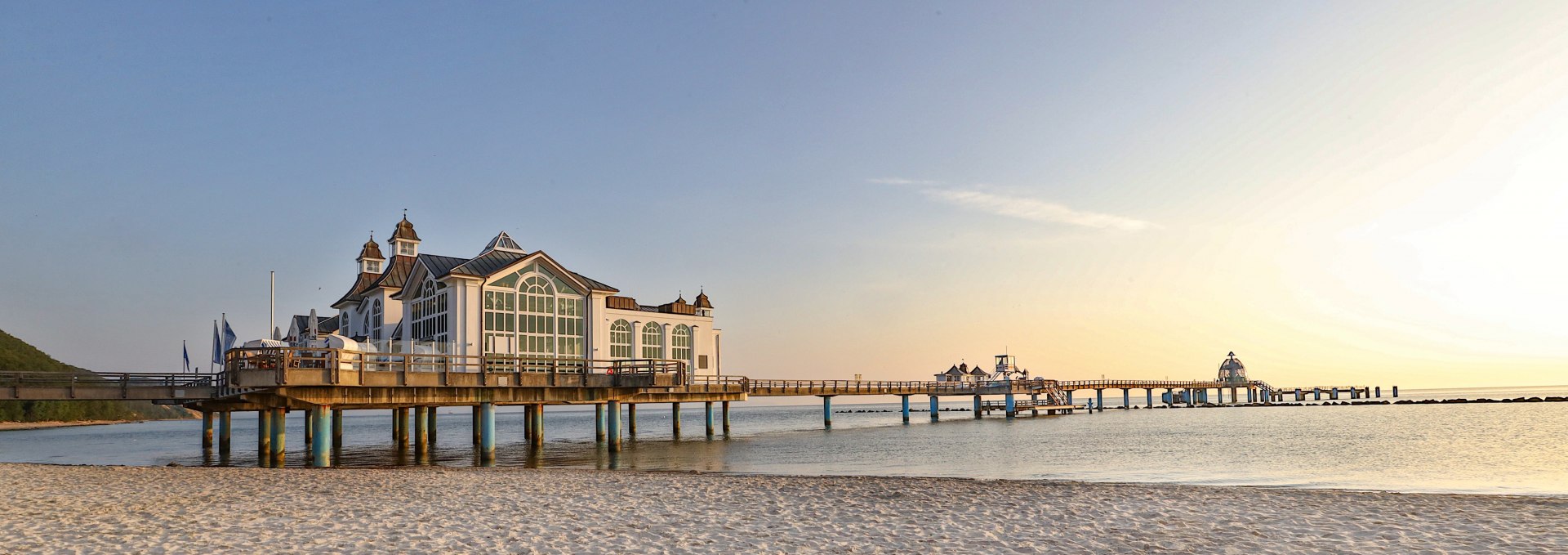 De pier in de Baltische badplaats Sellin bij zonsopgang, met een fijn zandstrand op de voorgrond en de kalme Baltische Zee op de achtergrond.
