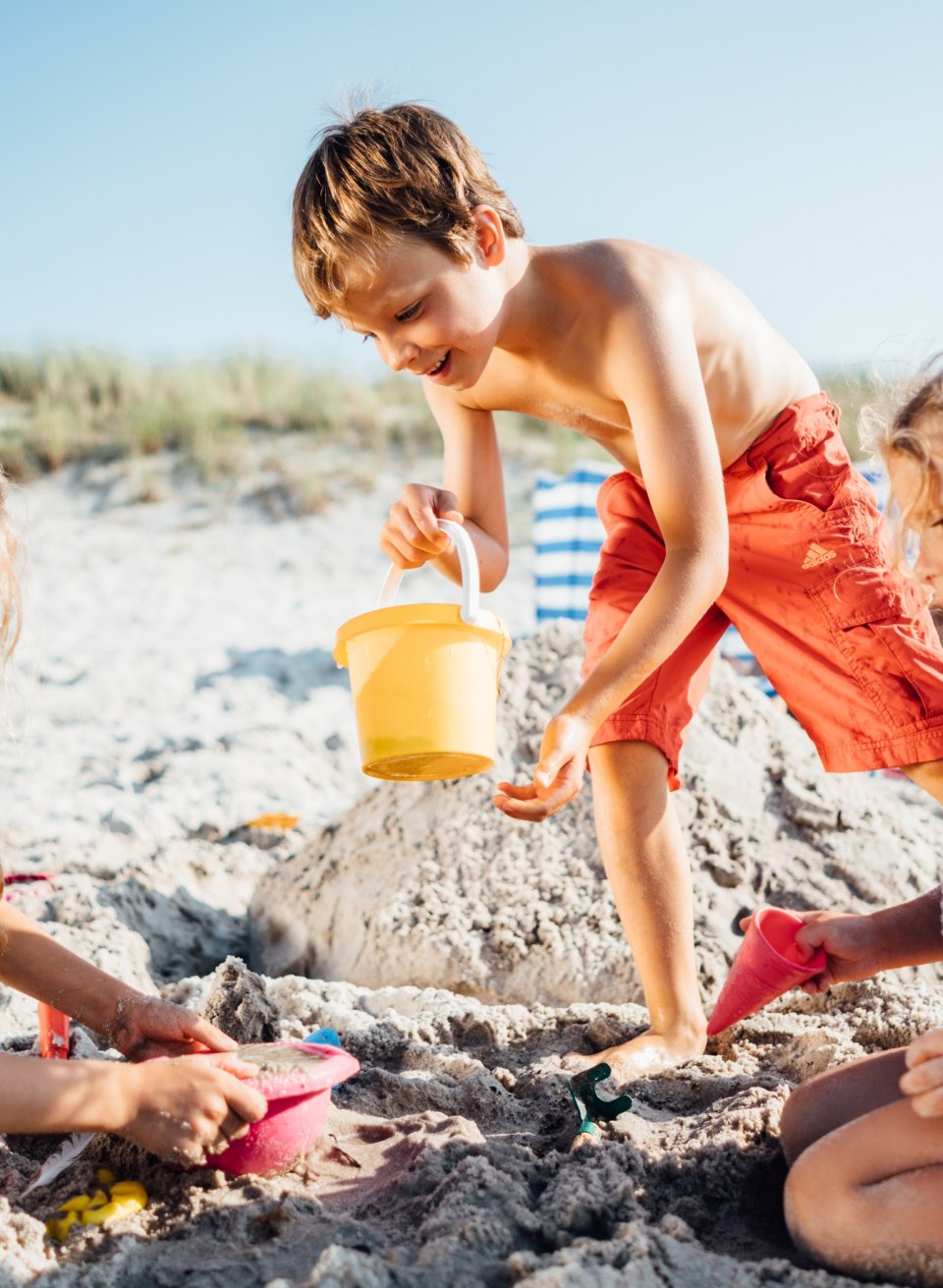 Drie kinderen spelen in het zand op het strand van Dierhagen, graven en bouwen samen in het felle zonlicht.