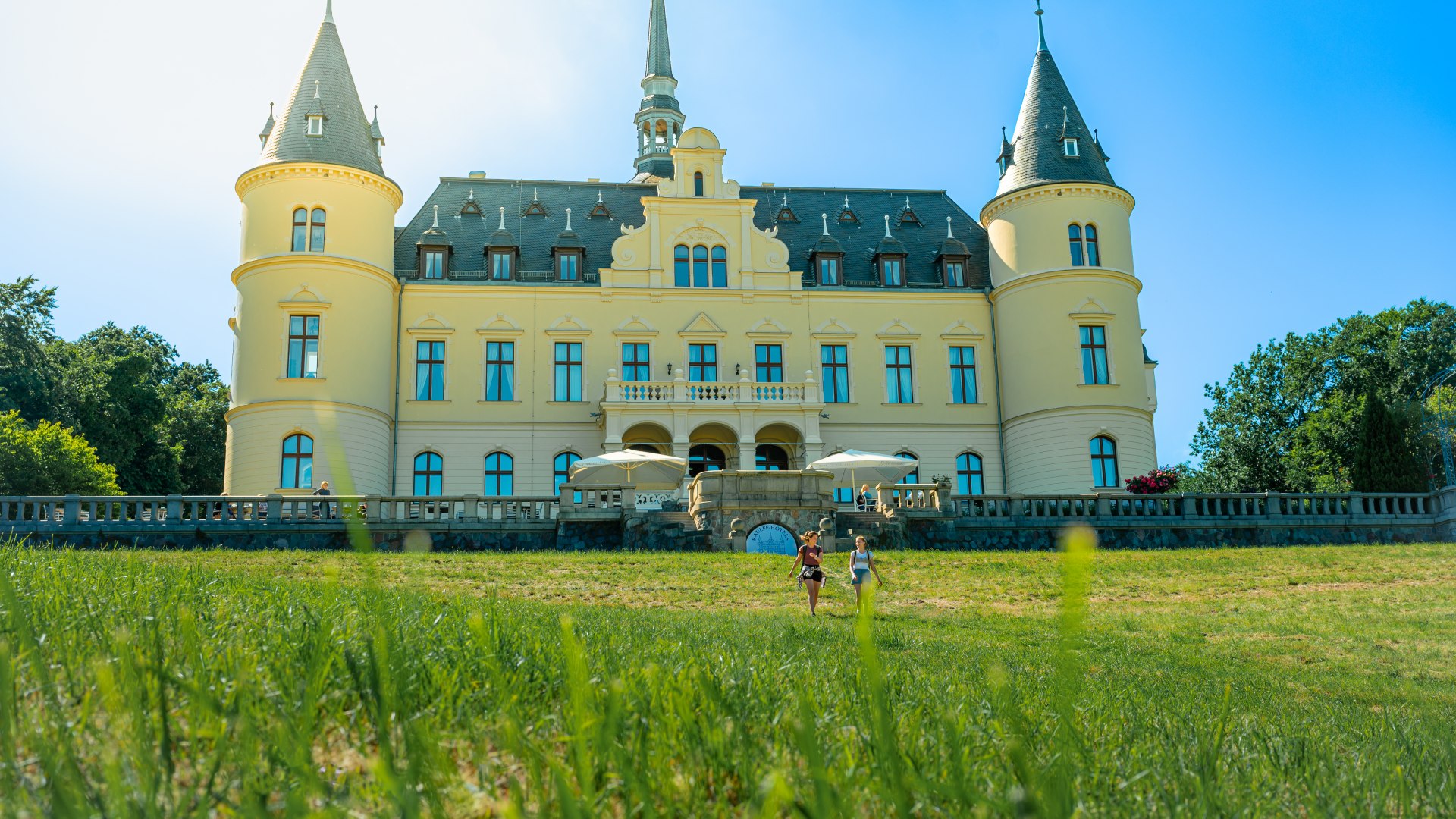 Two women walking in front of Ralswieck Castle // Built in 1896, Ralswiek Castle has served as a casino and retirement home over the years. Today there is a hotel behind the old walls. // © MV-T/Tiemann Two women walking in front of Ralswieck Castle