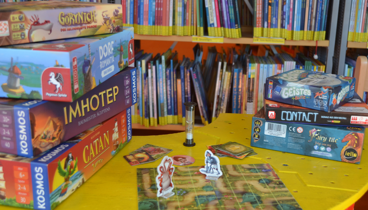 Several board games are lying on a yellow tabletop. A game board and two game pieces are set up., © Stadtbibliothek Stralsund