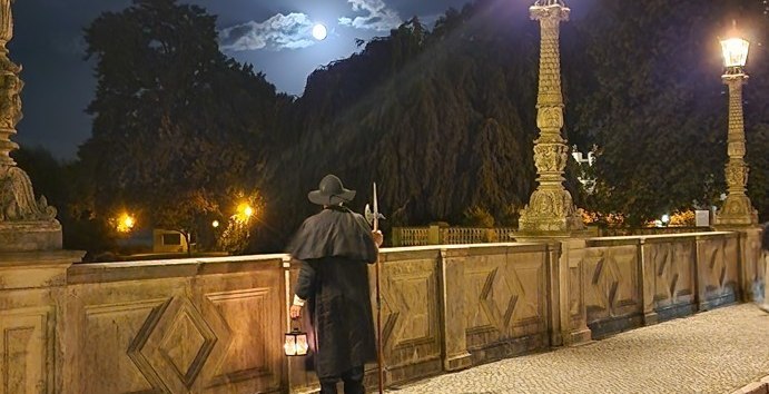 Nocny stróż na moście patrzący w stronę zamku nocą., © Michael Kratt