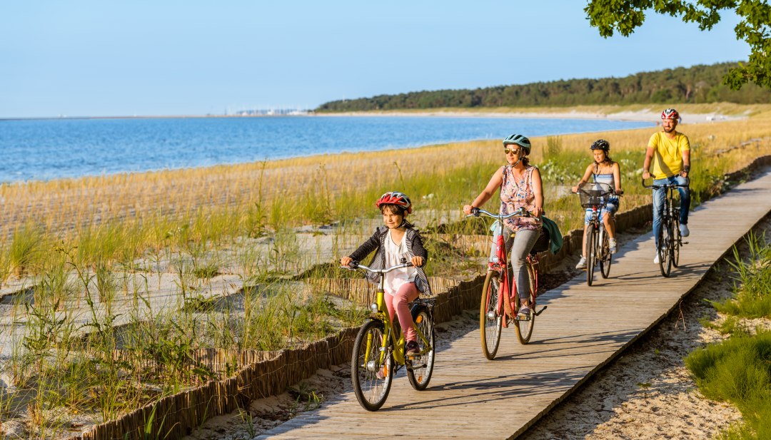 Een gezin van vier fietst over het fietspad op het strand.