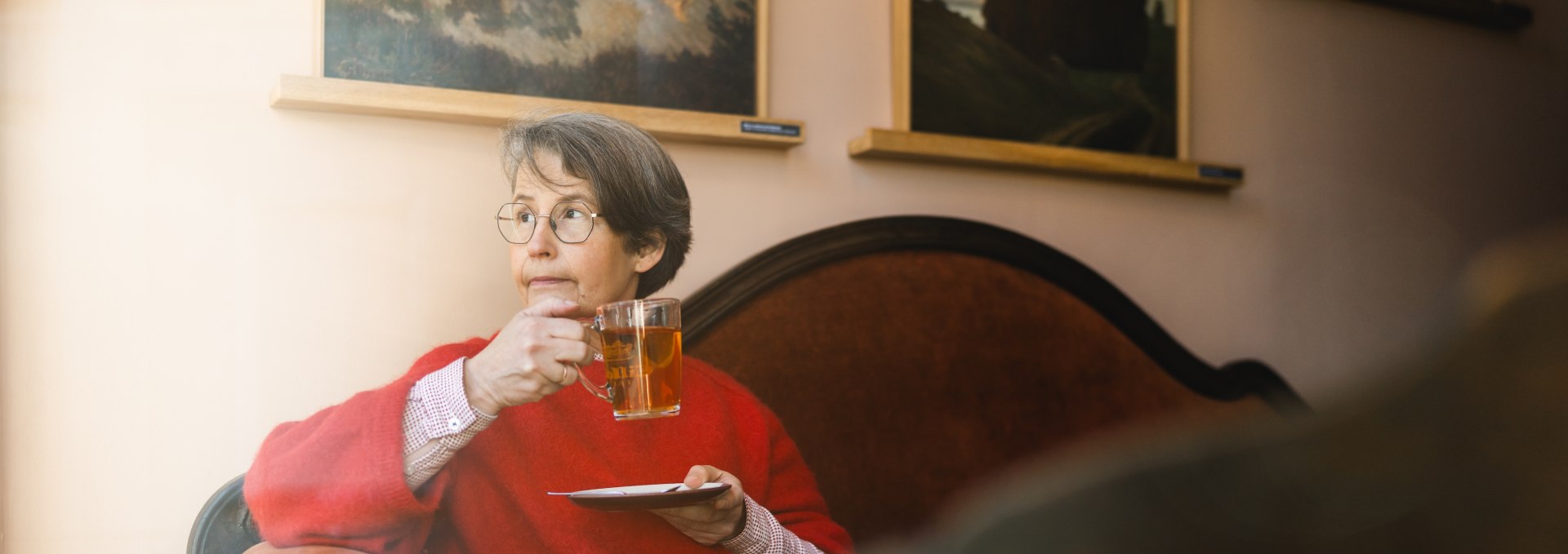Vrouw met thee in het gezellige Caf&eacute; Gertrud in Greifswald, omringd door kunstwerken aan de muren.