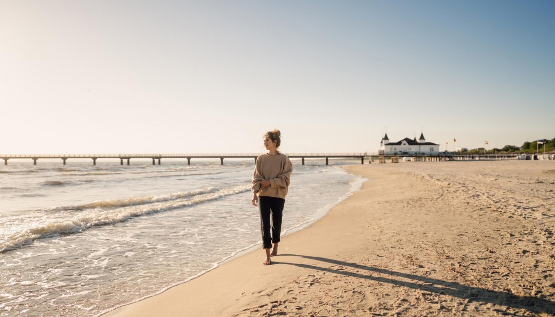 Wandelende vrouw op het strand van Ahlbeck bij zonsopgang met pier op de achtergrond