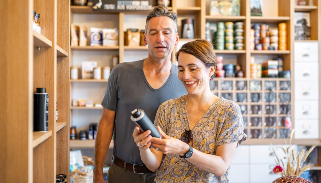 Smiling couple in a farm store, surrounded by shelves of regional products, examining an item.