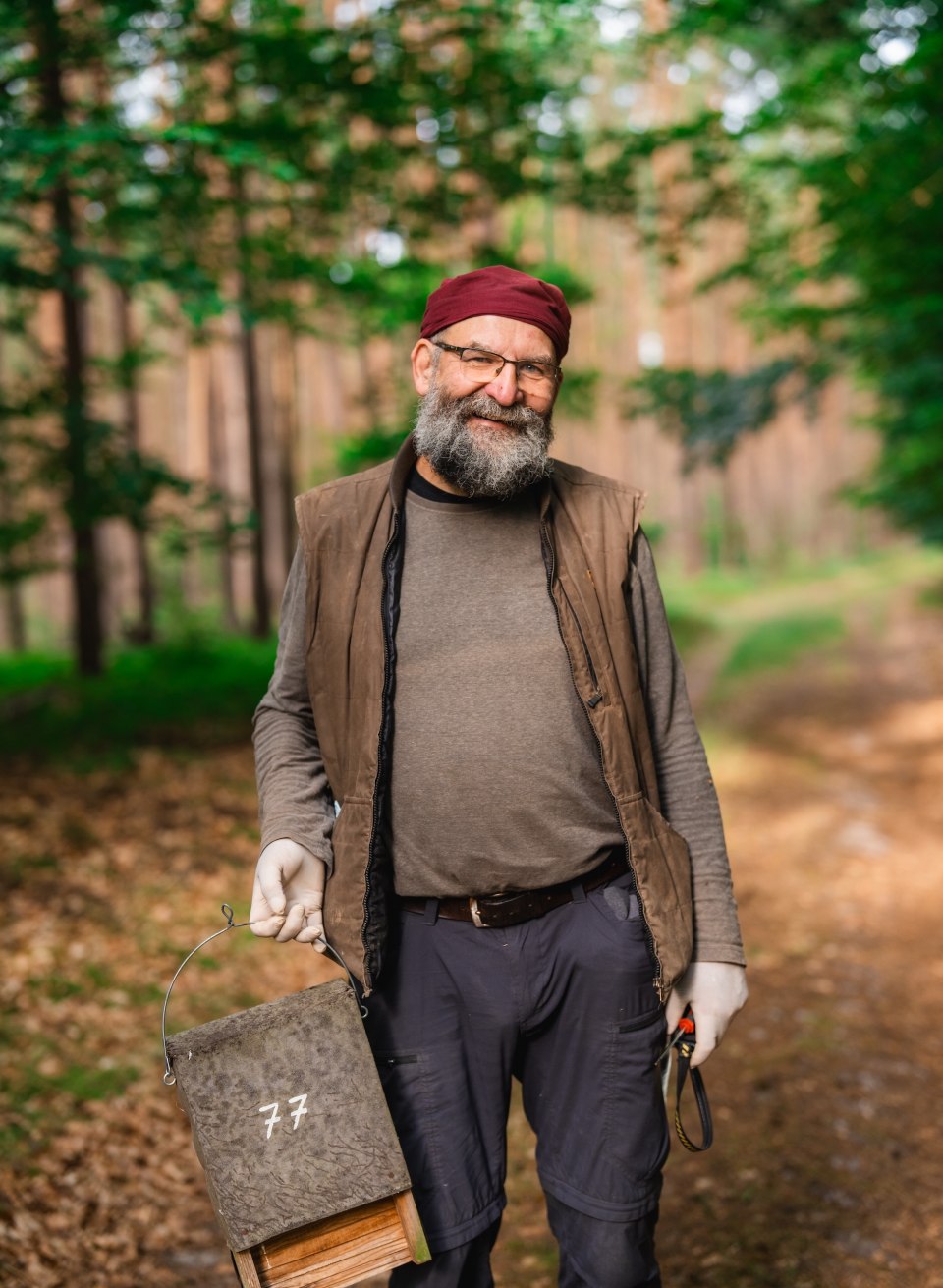 En mand står på en skovvej og holder en nummereret flagermuskasse i hånden, med træer i baggrunden. // Ralf Koch står på Waldweg, holder en flagermuskasse i hånden og gør sig klar til den næste kontrol – naturbeskyttelse, tydeligt og tæt på i Mecklenburg-Vorpommern. // © MV-T/Gross En mand står på en skovvej og holder en nummereret flagermuskasse i hånden, med træer i baggrunden.