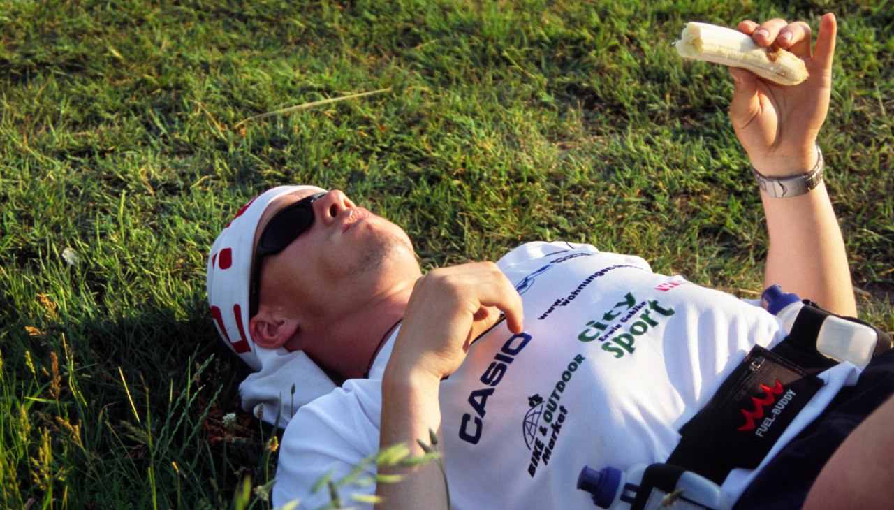 Ronald Prokein leżący na łące w stroju sportowym i okularach przeciwsłonecznych z bananem w dłoni, © Ronald Prokein