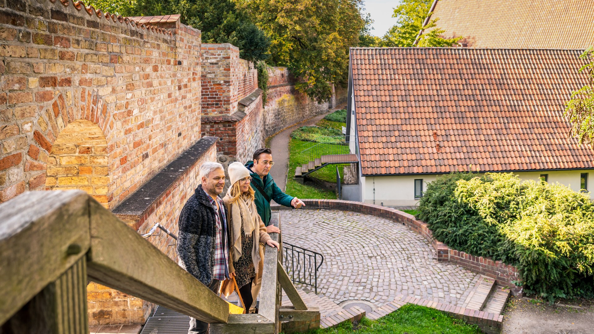 Drie mensen staan bij de oude stadsmuur in Rostock en kijken uit op de &quot;binnenplaats&quot;