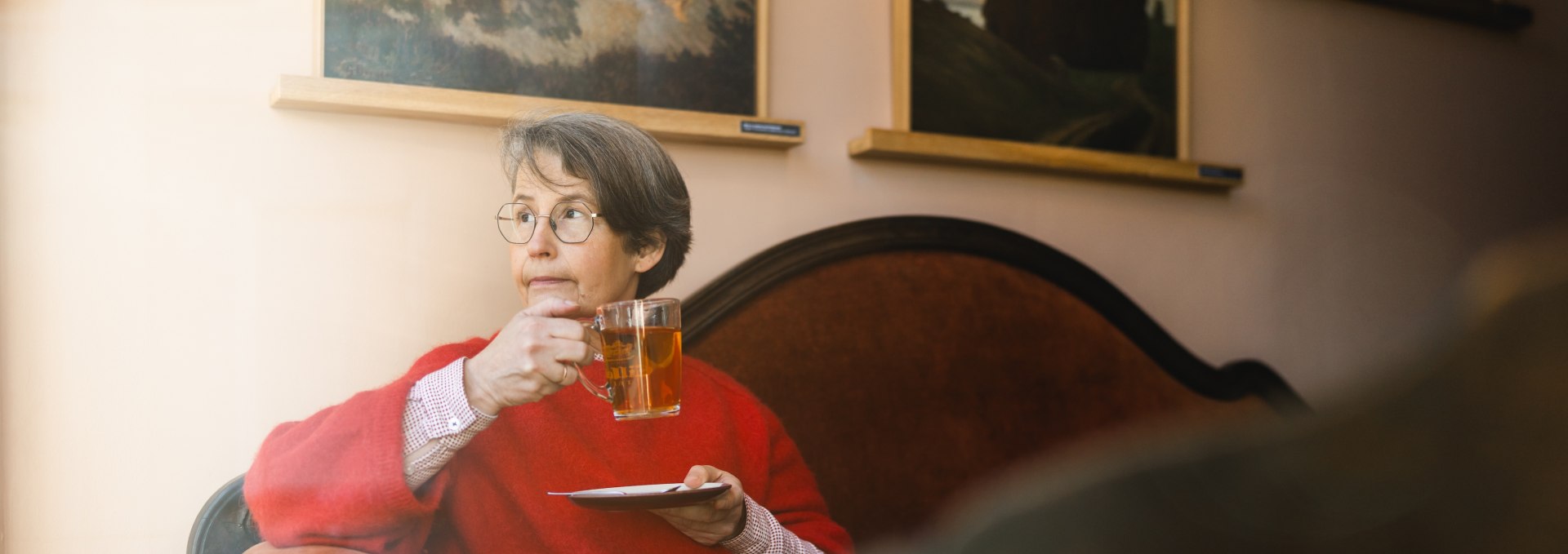 Vrouw met thee in het gezellige Caf&eacute; Gertrud in Greifswald, omringd door kunstwerken aan de muren.