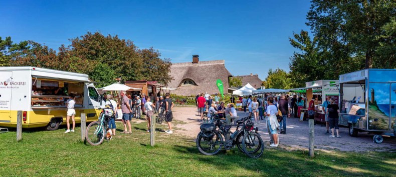 The Ahrenshoop summer market invites you to browse and enjoy in a relaxed atmosphere. Between traditional thatched cottages, regional traders present a wide range of products on their trailers - from fresh baked goods to organic delicacies. The picture shows the lively outdoor hustle and bustle, with visitors arriving by bike and lingering at small tables to experience the typical flair of the Baltic Sea region. // © Fa. Voigt & Kranz UG, Prerow The Ahrenshoop summer market invites you to browse and enjoy in a relaxed atmosphere. Between traditional thatched cottages, regional traders present a wide range of products on their trailers - from fresh baked goods to organic delicacies. The picture shows the lively outdoor hustle and bustle, with visitors arriving by bike and lingering at small tables to experience the typical flair of the Baltic Sea region. // © Fa. Voigt & Kranz UG, Prerow