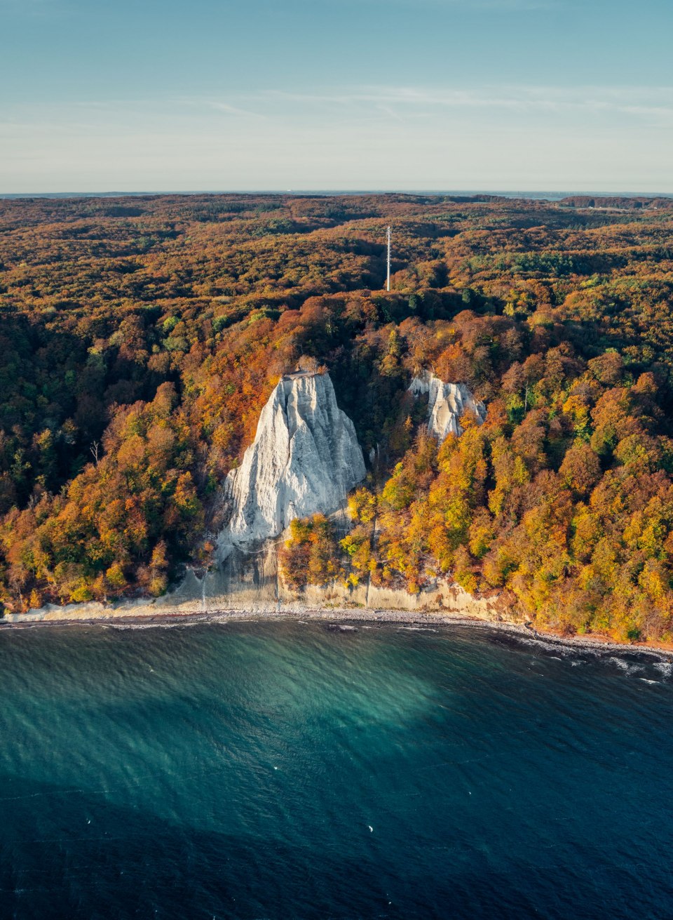 The imposing chalk cliffs in the Jasmund National Park glow in the morning autumn sun, surrounded by a sea of colorful foliage and the deep blue Baltic Sea - a breathtaking sight in the golden season., © TMV/Gänsicke The imposing chalk cliffs in the Jasmund National Park glow in the morning autumn sun, surrounded by a sea of colorful foliage and the deep blue Baltic Sea - a breathtaking sight in the golden season.