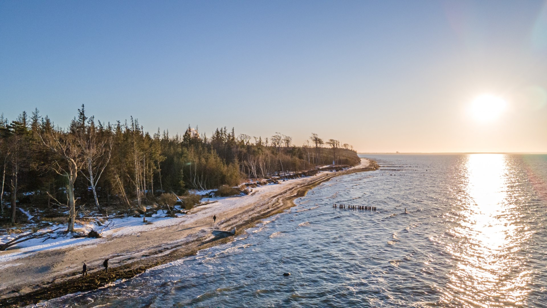 Winterstrand bij Torfbrücke Graal-Müritz met besneeuwde bomen, glinsterende Baltische Zee en een zonsondergang aan de horizon.
