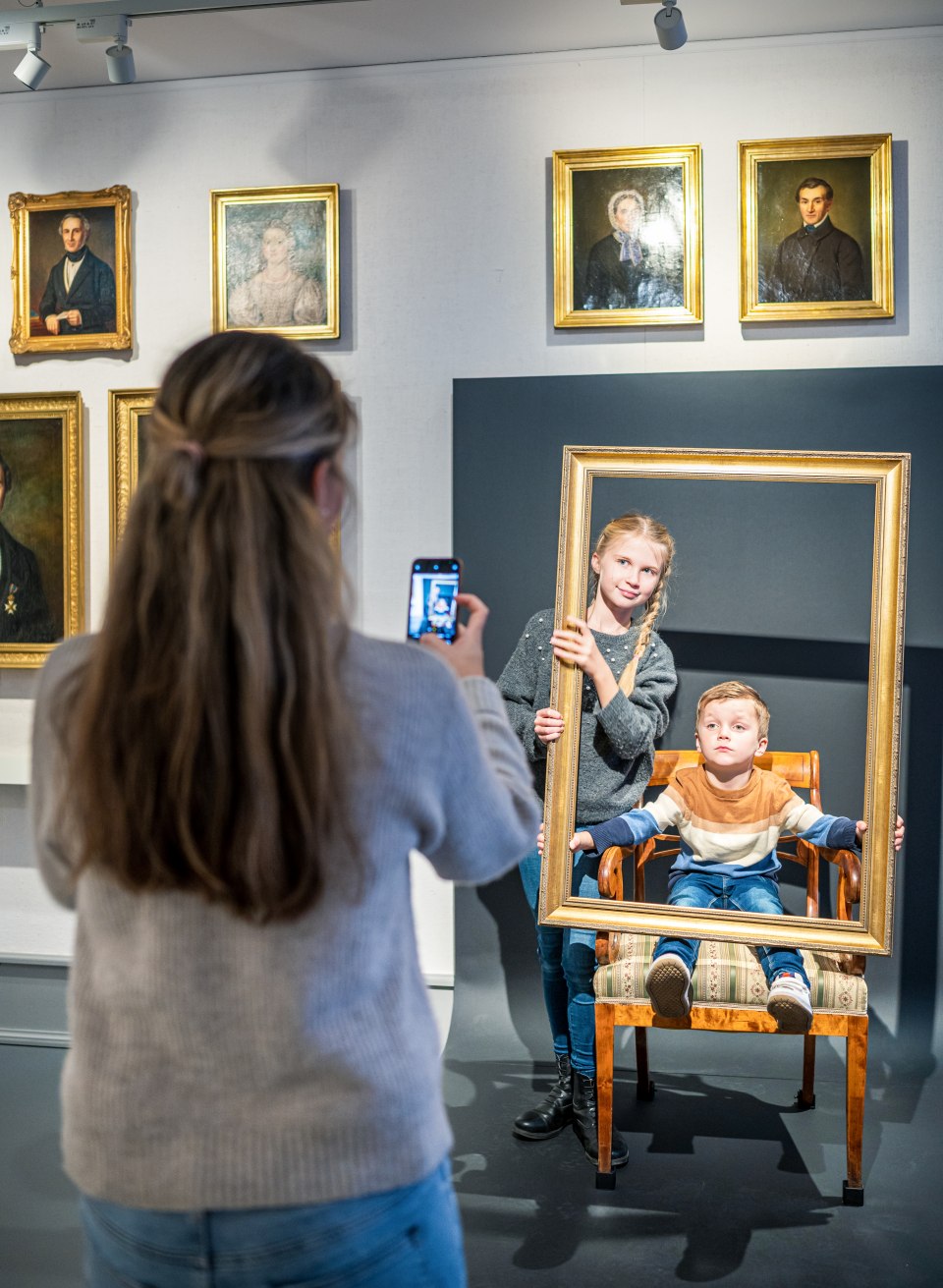 de nakomeling lacht vriendelijk vanuit een gouden fotolijstje - voor het portret in olie, sorry: souvenirfoto, © TMV/Tiemann