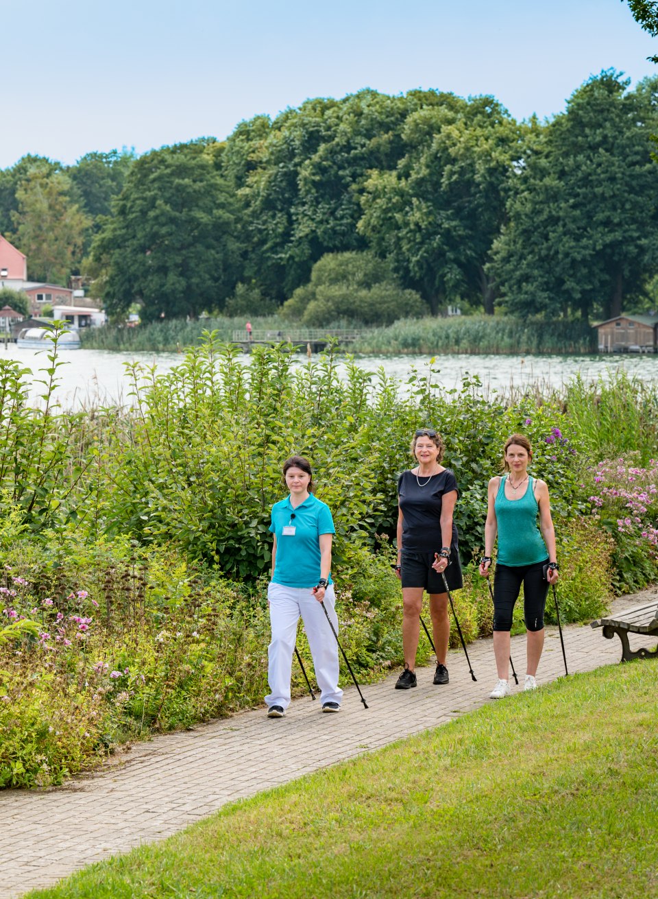 Trzy kobiety uprawiają nordic walking w parku przy jeziorze należącym do Medical Wellness Centre.