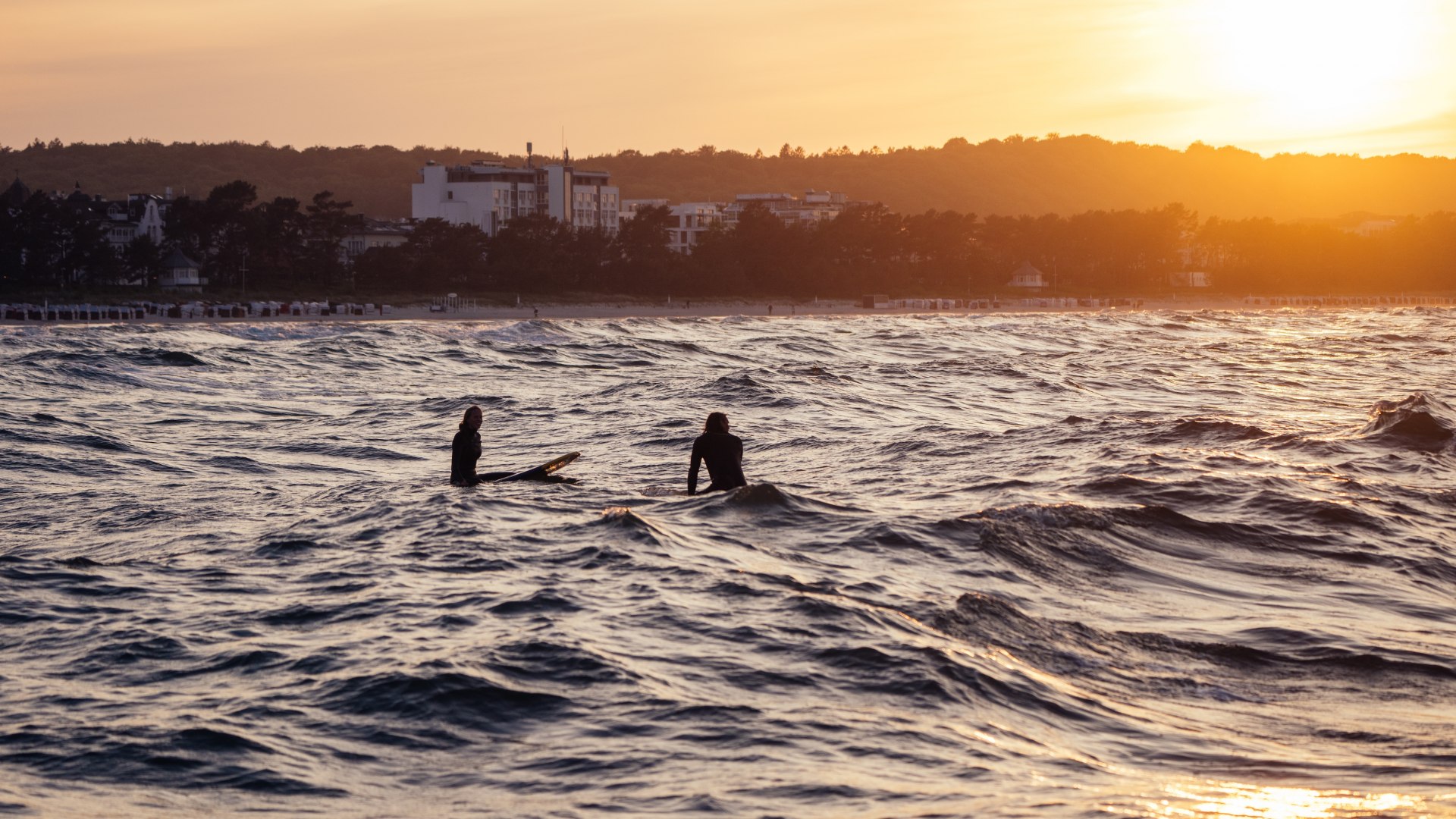 Dw&oacute;ch surfer&oacute;w na Morzu Bałtyckim w pobliżu Binz podczas nastrojowego zachodu słońca.
