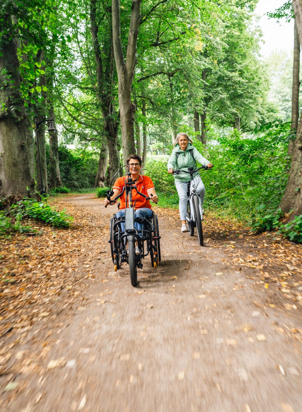 Elektrische handbike en fietser rijden over een bospad.