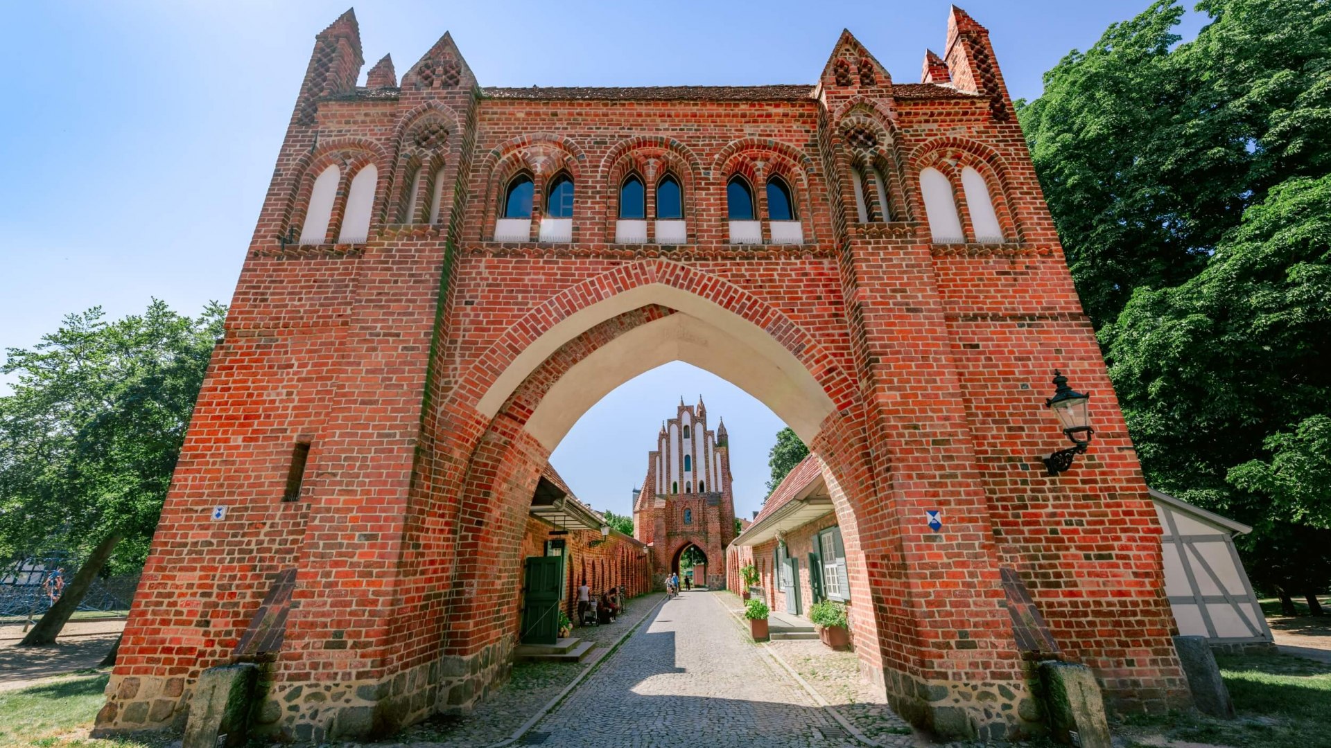 Widok przez jedną z bram miasta Neubrandenburg. Rowerzyści zbliżają się do Ciebie. // Co za wejście! Jedna z czterech średniowiecznych bram miejskich Neubrandenburga // © MV-T/Tiemann Widok przez jedną z bram miasta Neubrandenburg. Rowerzyści zbliżają się do Ciebie.