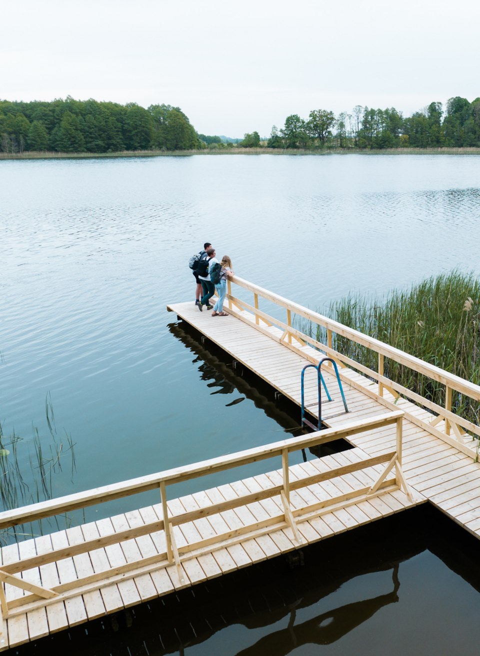 And a beaver actually swims past! Not far from the jetty on Lake Groß Raden, a beaver family has built its lodge., © TMV/Gross Three friends stand on the jetty on Lake Groß Raden and look out over the water