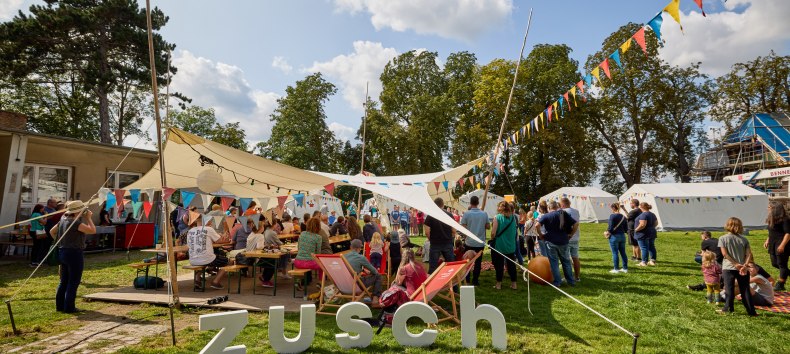 People stand under an awning decorated with colorful pennants // © Oliver Borchert People stand under an awning decorated with colorful pennants // © Oliver Borchert