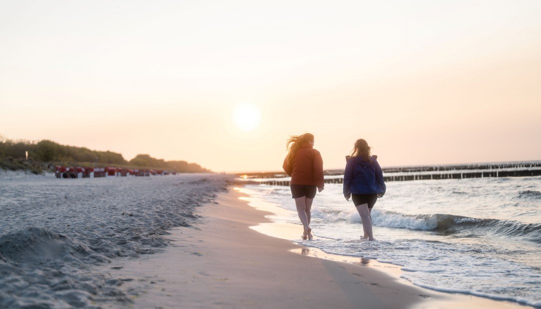 Twee vrouwen lopen op blote voeten langs de Baltische Zee bij zonsondergang op het strand in Koserow.