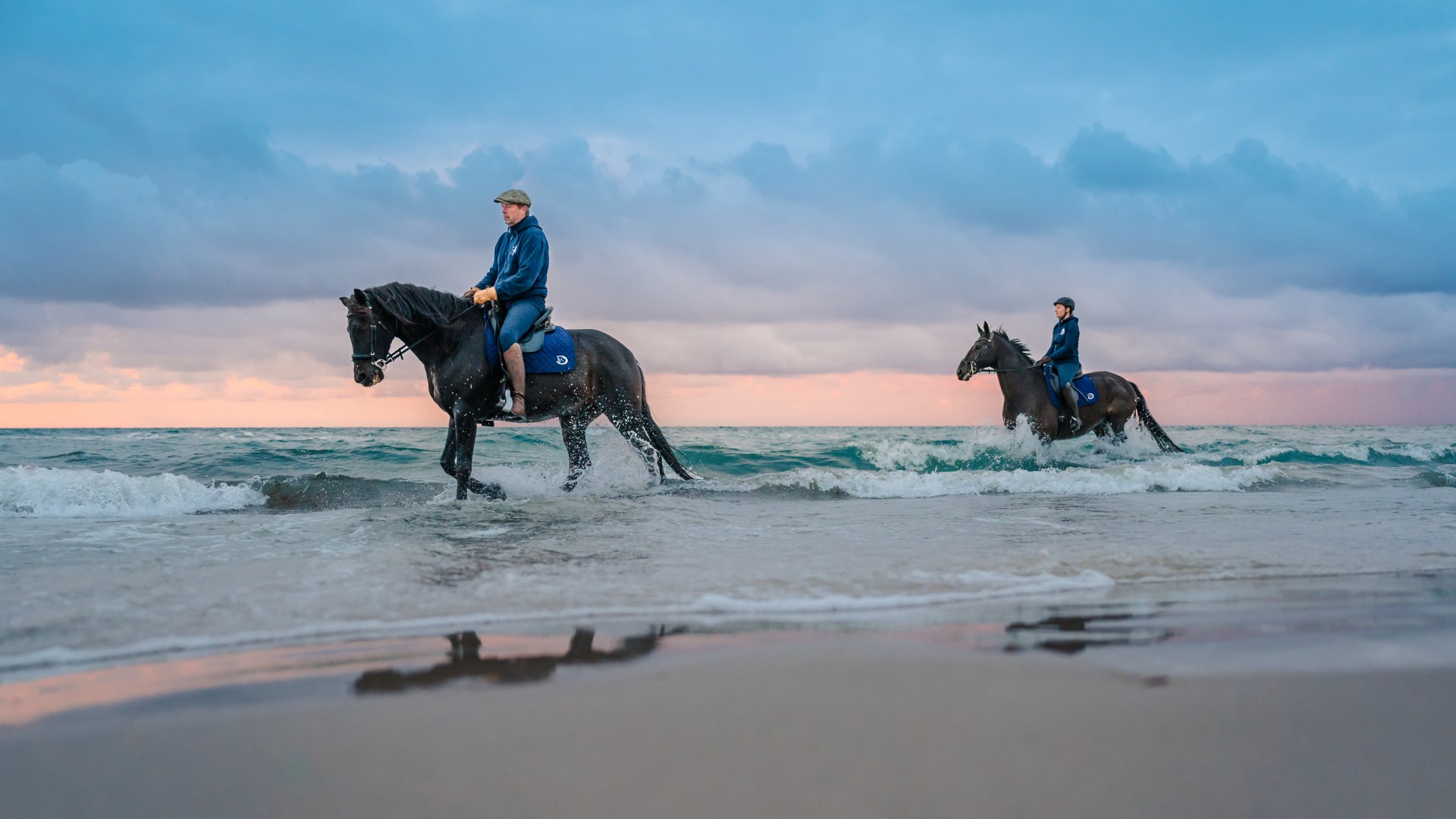 Twee ruiters te paard gaan strandrijden bij zonsondergang aan de Oostzee op het schiereiland Fischland-Darß-Zingst