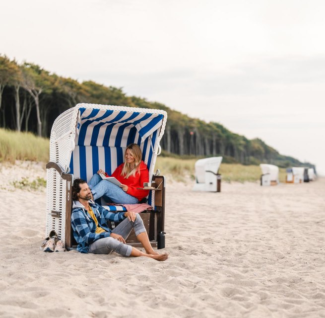 Couple sitting in a beach chair on the beach at Graal-Müritz on the Baltic Sea coast. The coastal forest can be seen in the background.