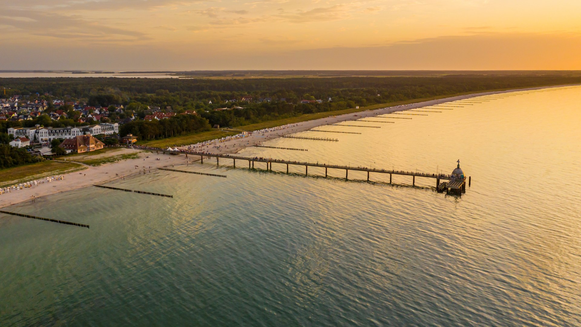 Aerial view of the Zingst pier with a view of the Baltic Sea beach and the setting sun on the horizon.
