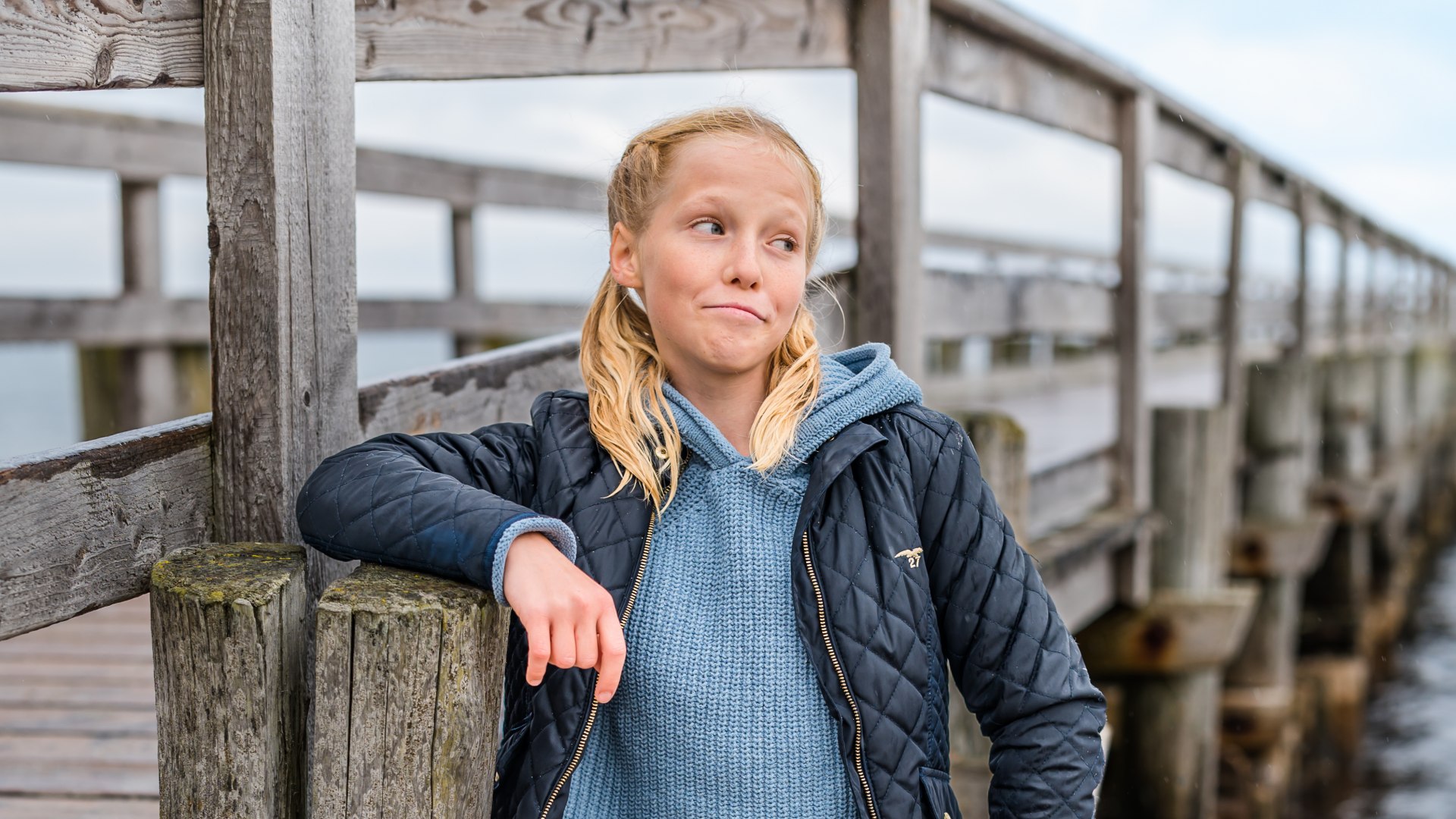 Portret van Madita von Klitzing leunend op het strand tegen het hout van de pier in Zingst met de Baltische Zee op de achtergrond.