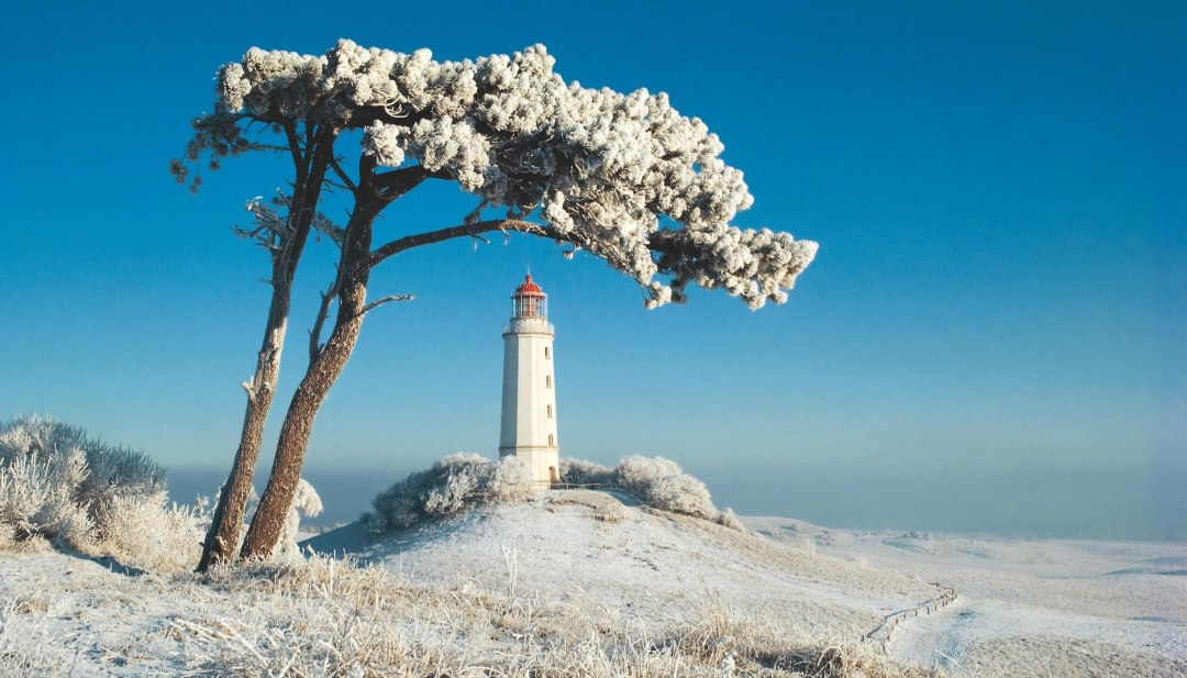Snow-covered lighthouse at Dornbusch on Hiddensee, surrounded by a frosty winter landscape under a bright blue sky.