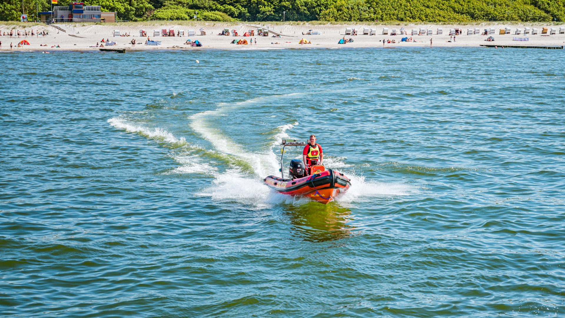 DLRG motorboot met strandwacht varend op de Oostzee bij Graal-Müritz met het strand op de achtergrond.
