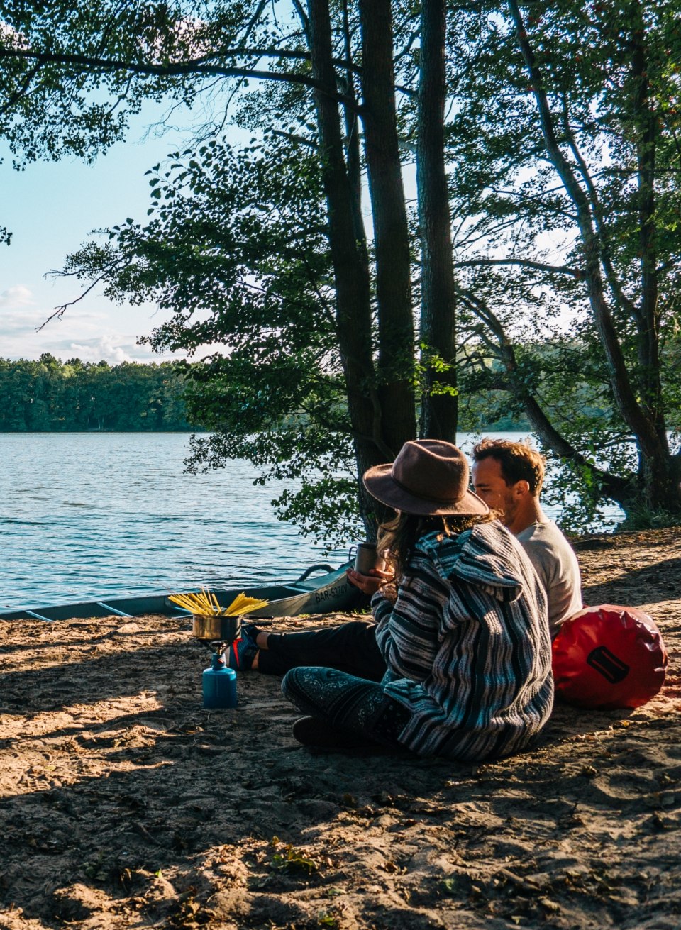 Para siedzi nad wodą z kuchenką gazową i gotuje makaron na kempingu Hexenw&auml;ldchen