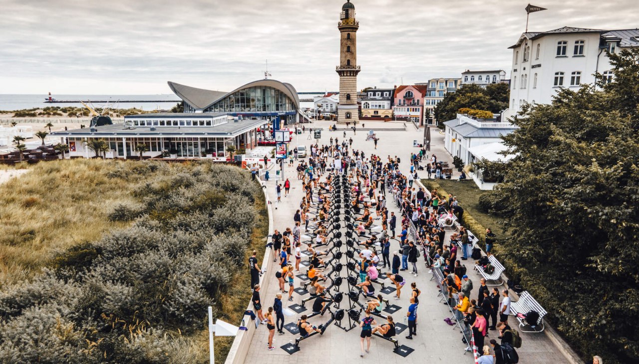 Rowing competition in front of the Warnemünde lighthouse on the promenade with rowing ergometers at the Battle The Beach fitness competition., © TMV/Witzel Rowing competition in front of the Warnemünde lighthouse on the promenade with rowing ergometers at the Battle The Beach fitness competition., © TMV/Witzel