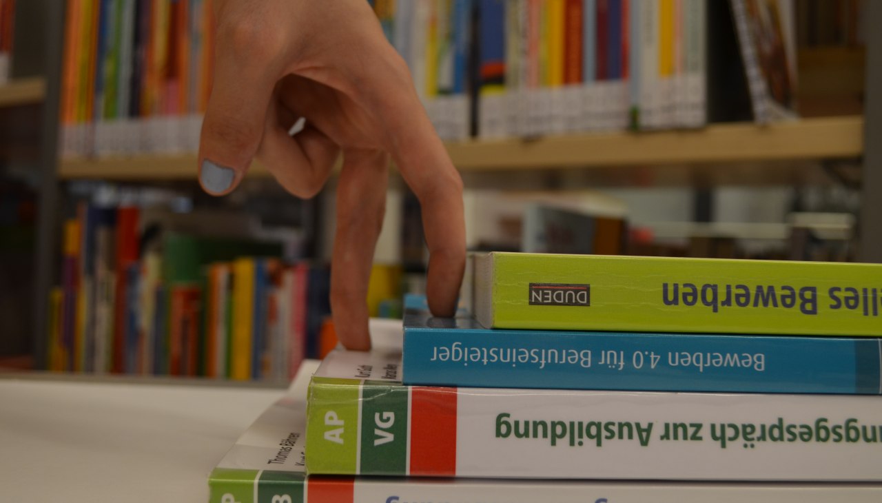 Dwa palce symbolicznie wspinają się po schodach wykonanych z książek, © Stadtbibliothek Stralsund