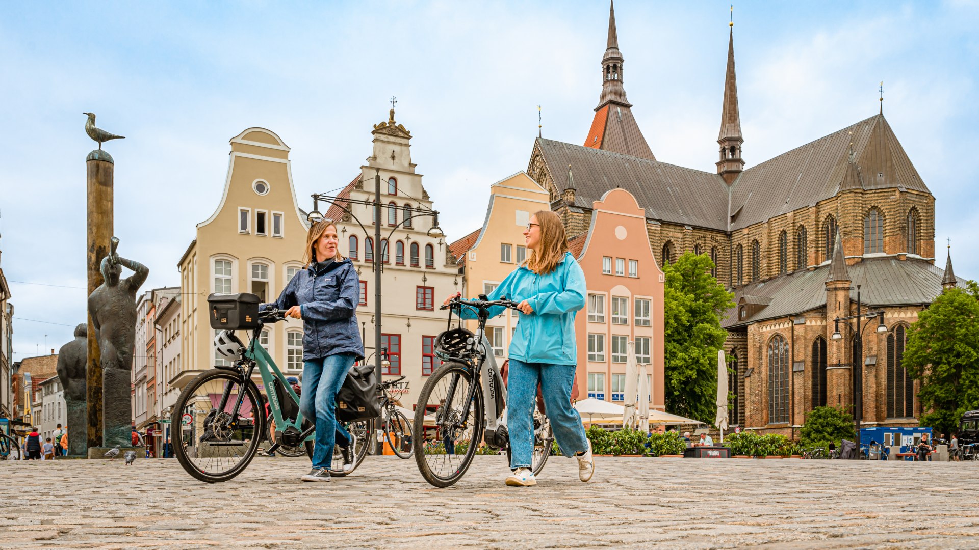 Moeder en dochter duwen hun fietsen over het marktplein van Rostock